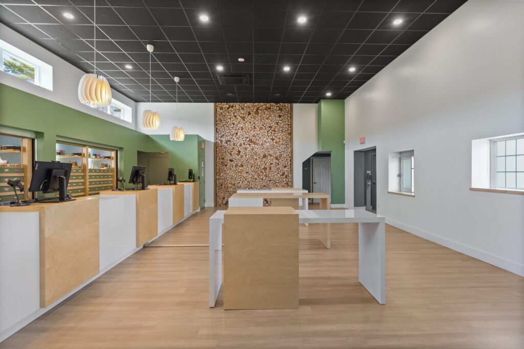 Modern retail interior designed by Blue Anchor Design featuring wood and white service counters, pendant lighting, green accent walls, and a stacked firewood display.